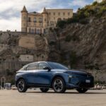 2026 Lancia Gamma front three-quarters fastback crossover at seaside Italian harbor