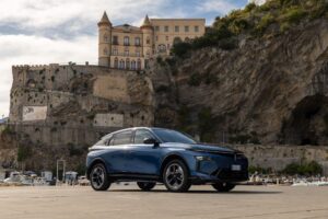 2026 Lancia Gamma front three-quarters fastback crossover at seaside Italian harbor